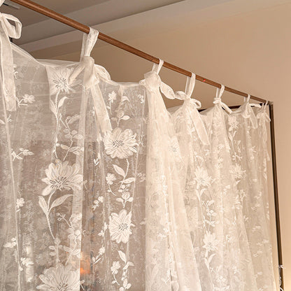 Sheer floral curtains with a wooden rod against a beige wall.