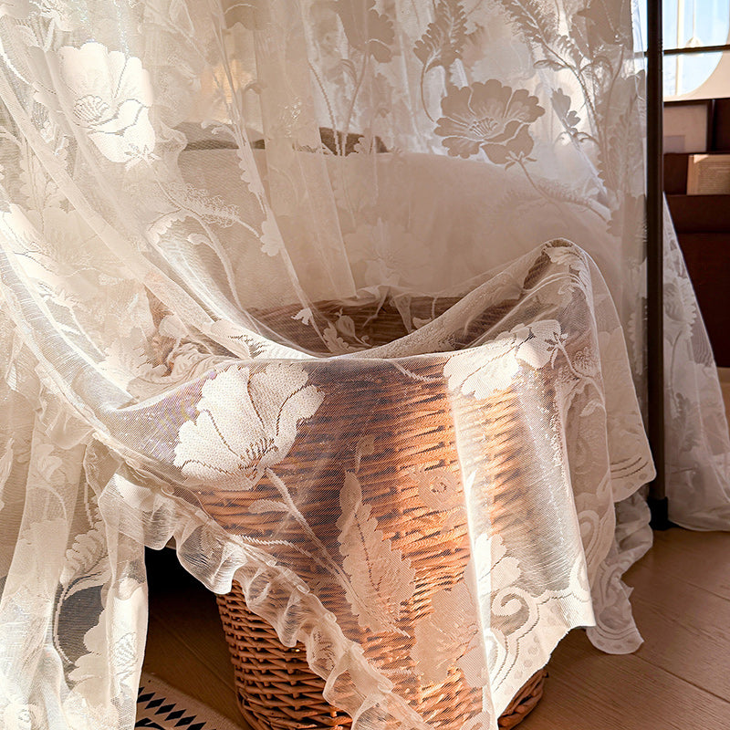 Floral lace curtain draped over a wicker basket on a wooden floor.