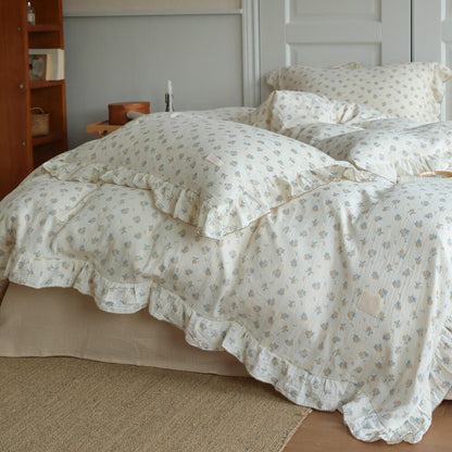 Ruffled cotton muslin blue rosebud duvet cover set displayed on an ivory bed with matching pillows