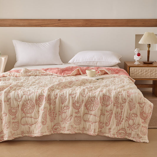 Sea life cotton blanket styled on bed with coral-pink and ivory reversible jacquard design