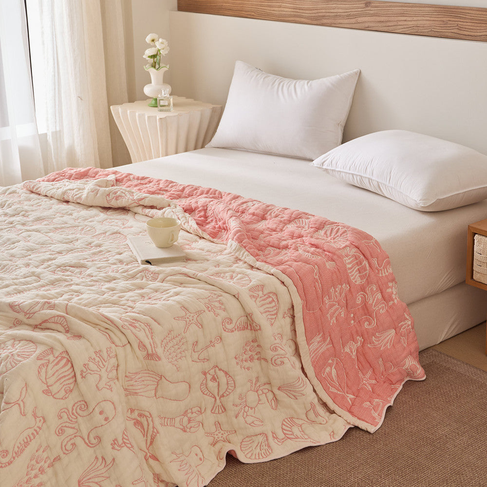 Sea life cotton blanket layered on bed with muted sea-green reversible side and shell motifs