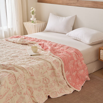 Sea life cotton blanket layered on bed with muted sea-green reversible side and shell motifs