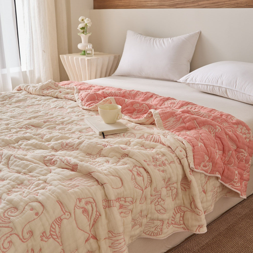 Reversible sea life cotton blanket on bed with coral-pink side, ivory side, and cup styling