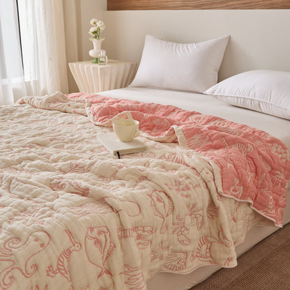 Reversible sea life cotton blanket on bed with coral-pink side, ivory side, and cup styling