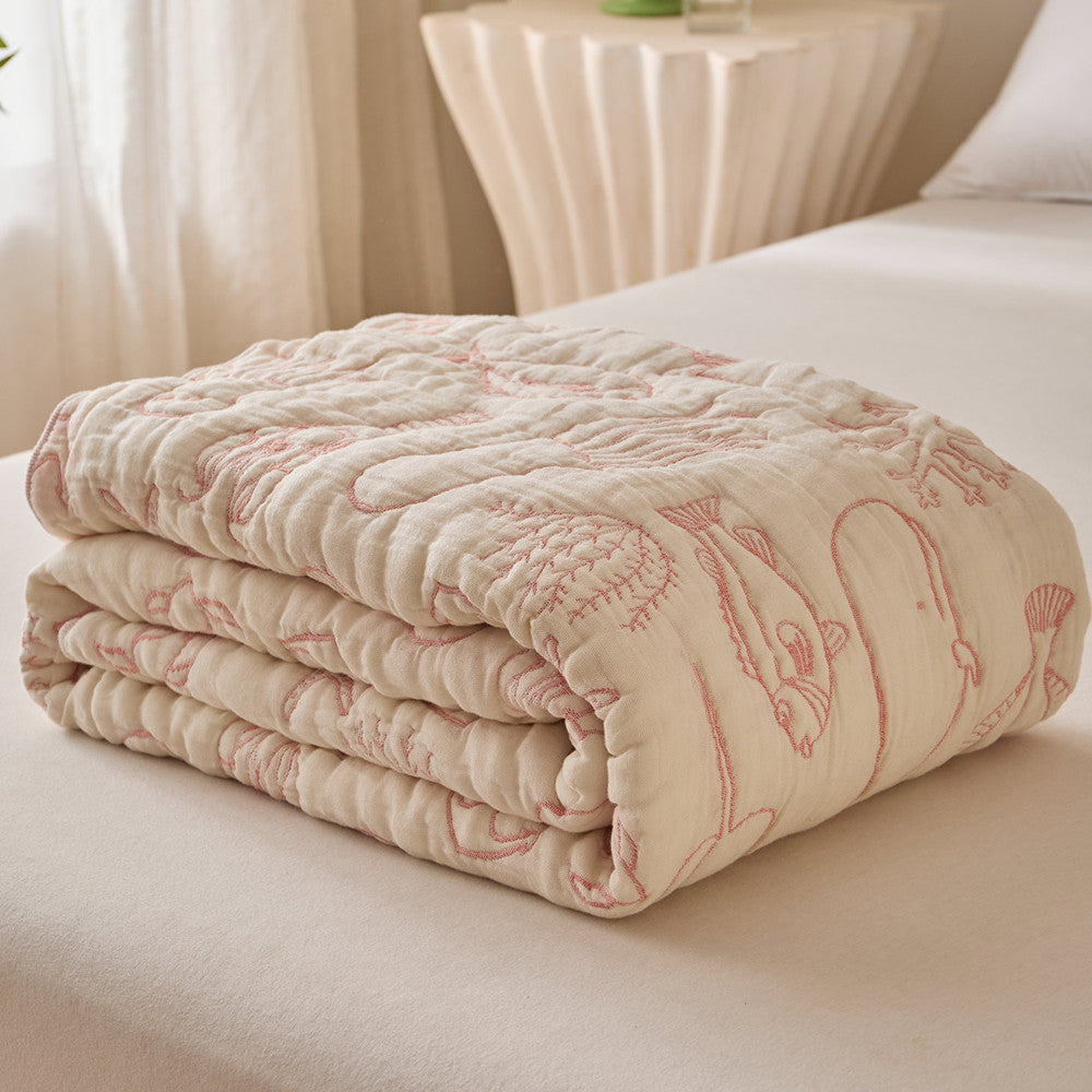 Folded sea life cotton blanket showing ivory muslin fabric with coral-pink jacquard motifs