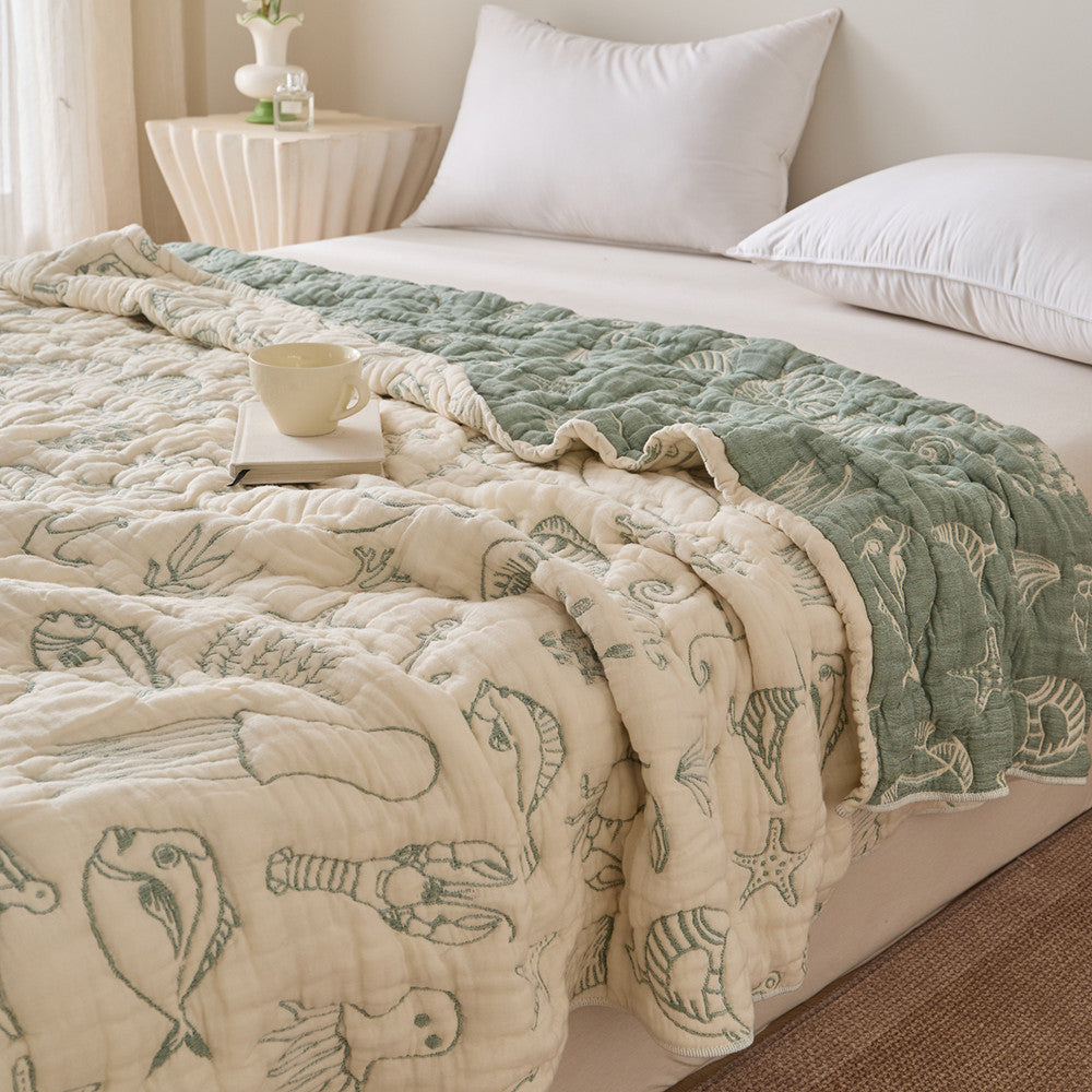 Sea life cotton blanket styled on bed with sage green reverse side and ivory front