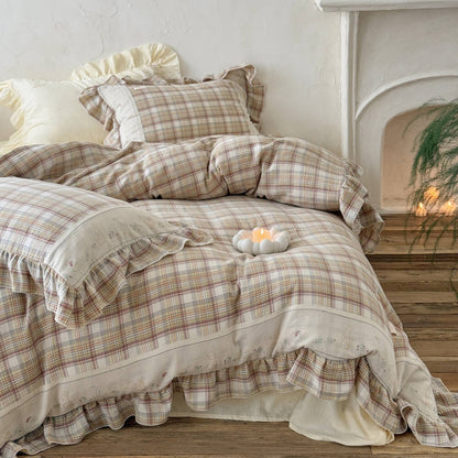 Plaid cotton muslin bedding set with ruffled edges, arranged on a bed near a white fireplace for a soft cottage look