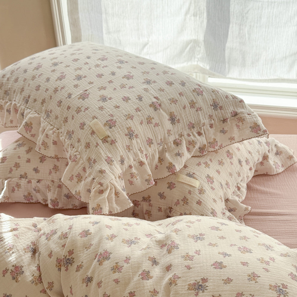 Stacked ruffled pillow shams from the Tuberose Floral Cotton Duvet Cover Set, featuring the subtle, vintage-inspired flower print and detailed ruffle trim, set near a sunny window.
