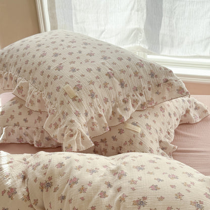 Stacked ruffled pillow shams from the Tuberose Floral Cotton Duvet Cover Set, featuring the subtle, vintage-inspired flower print and detailed ruffle trim, set near a sunny window.