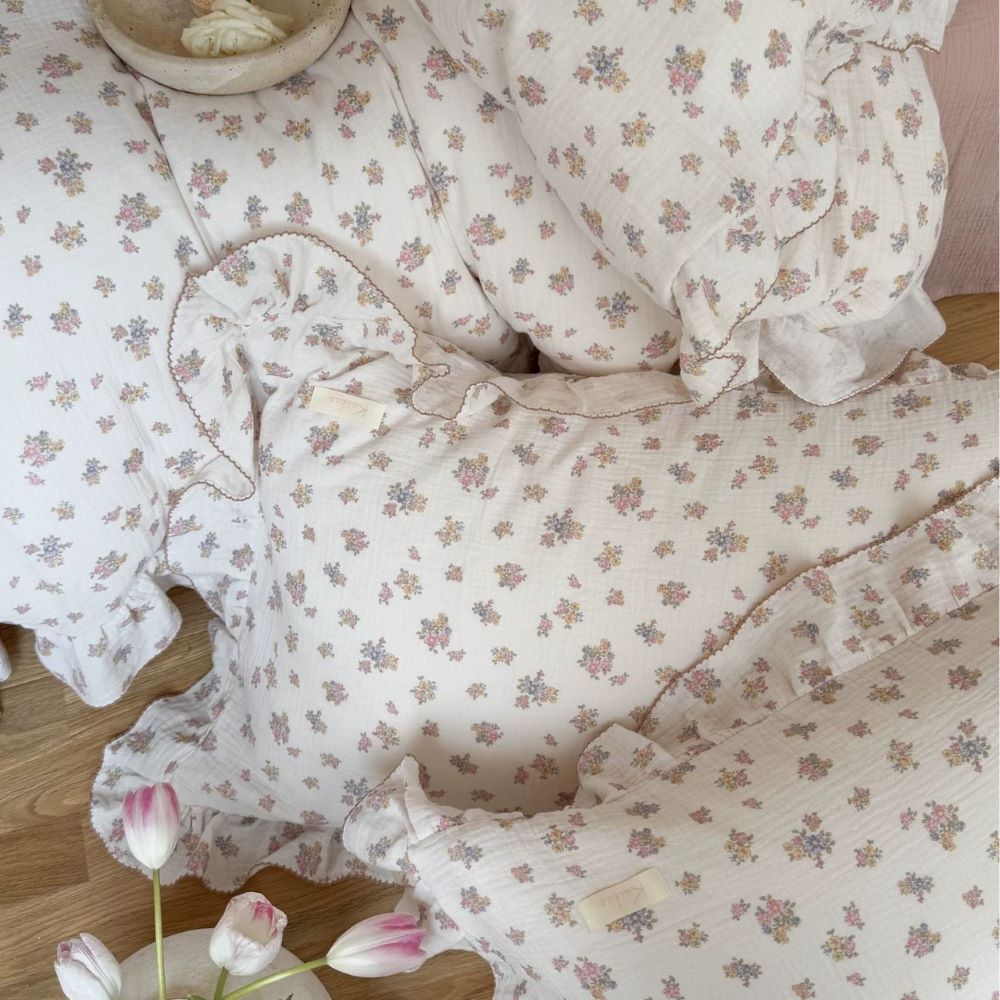 Overhead view (flat lay) of the Tuberose Floral Cotton Muslin Duvet Cover and multiple ruffled pillow shams, showing the complete floral pattern and soft, wrinkled gauze texture up close.