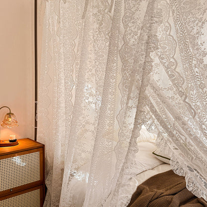 Lace curtains in a bedroom with a wooden nightstand and lamp.