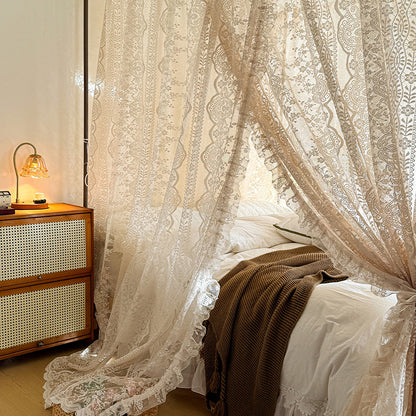 Lace curtains in a bedroom with a wooden nightstand and lamp.