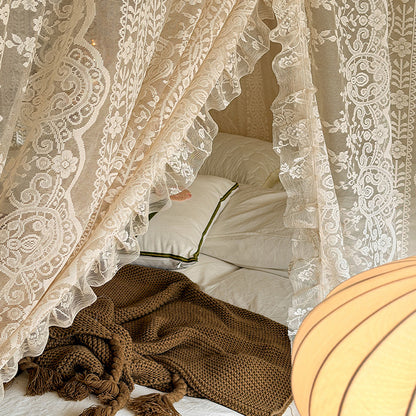 Bed with lace curtains and a brown blanket, warm lighting.