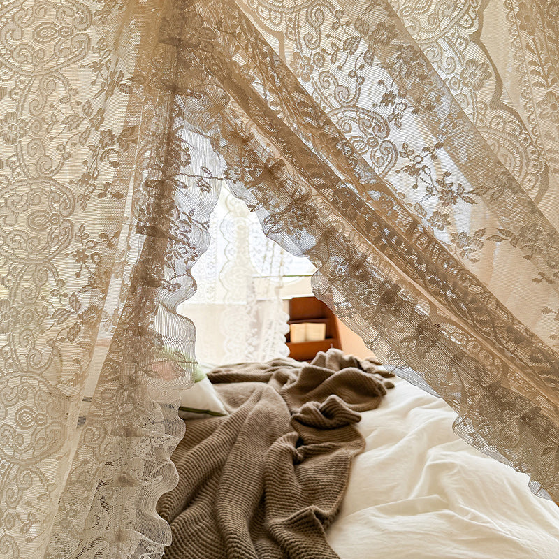 Decorative lace curtains with a patterned curtain partially open, revealing a soft light.