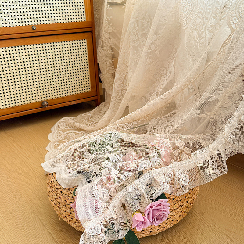 Lace fabric draped over a woven basket with flowers on a wooden floor.