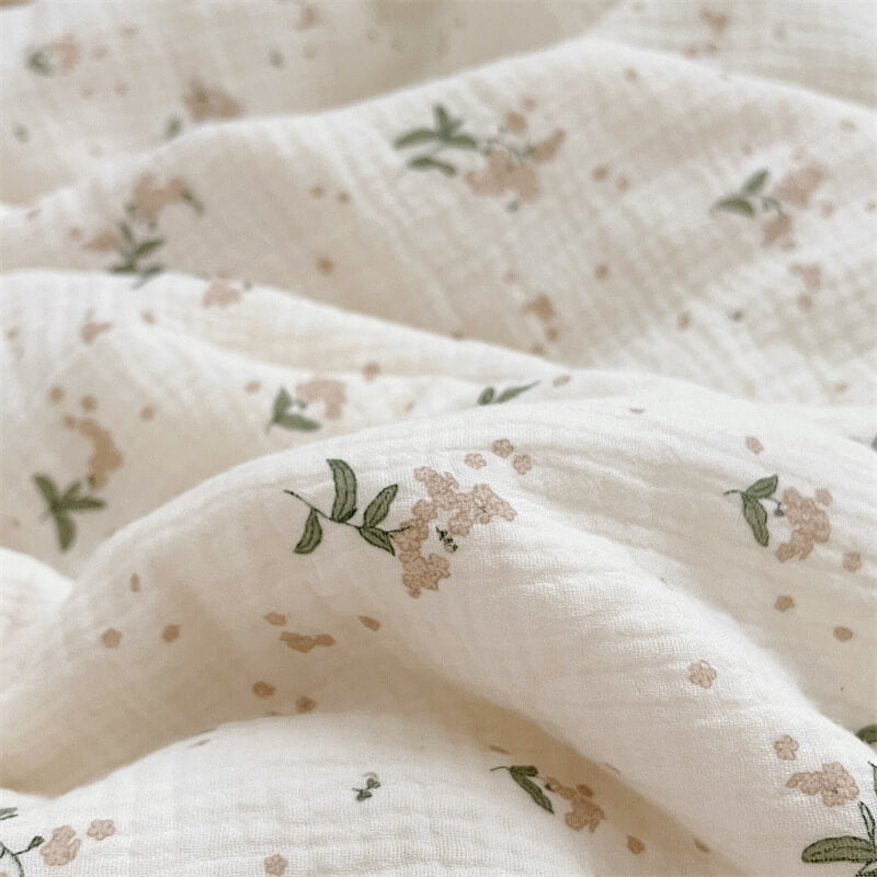 Close-up shot of a crinkled cotton muslin baby blanket with a delicate floral print.