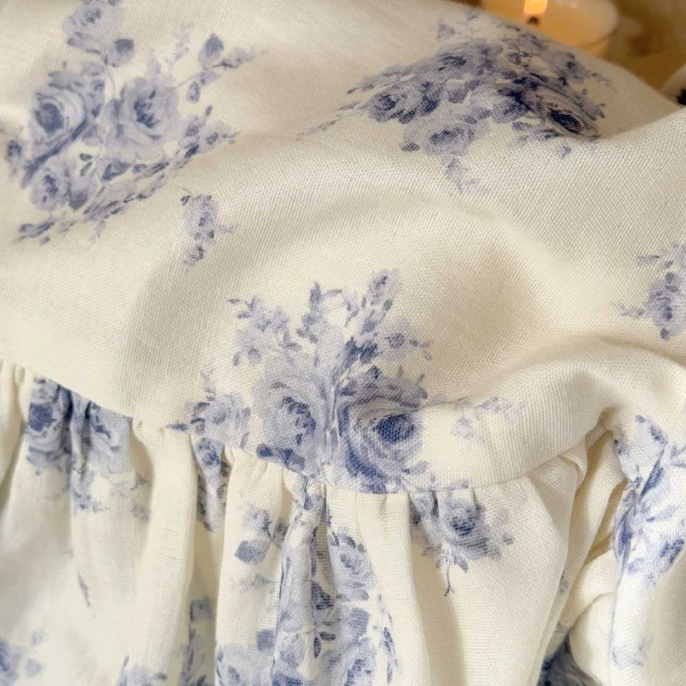 Detailed macro shot of the cotton muslin fabric, showing the fine texture and the delicate blue floral print on the ruffle trim of the bedding set.