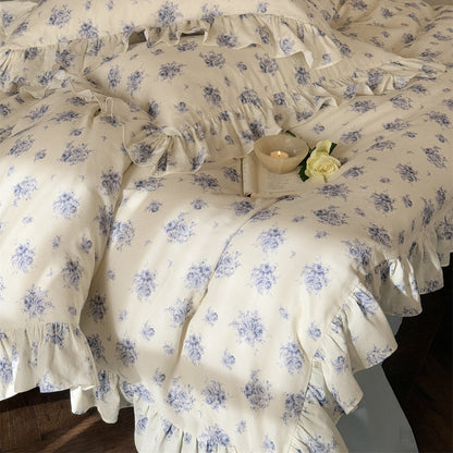 Close-up of a soft and breathable cotton muslin bedding set, featuring a dusty blue floral pattern and romantic ruffle trim on the duvet cover and pillows.