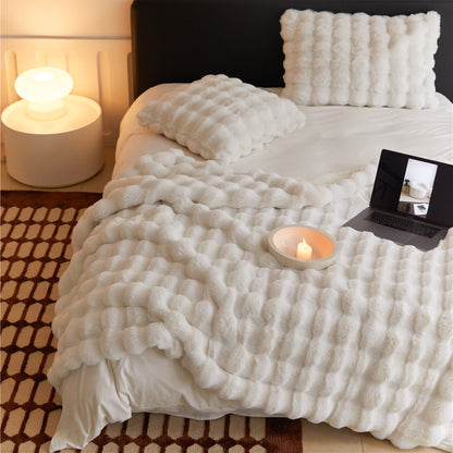 Fluffy off-white faux rabbit fur throw blanket styled on a bed with matching pillows.