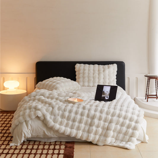 Soft off-white textured faux rabbit fur blanket and pillows on a bed with a laptop