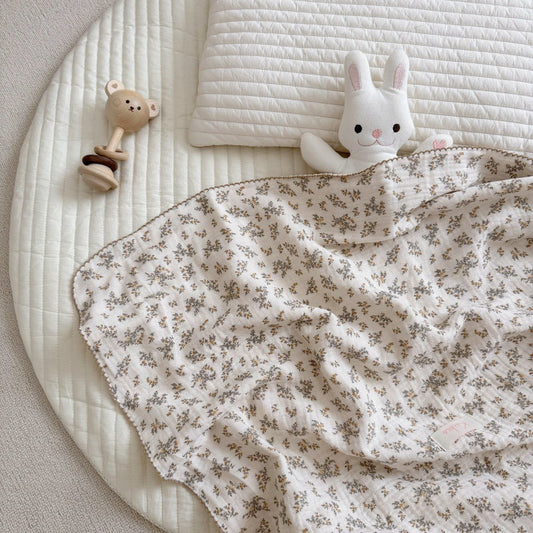 An Osmanthus floral print crinkled muslin baby blanket on a baby cot, with small teddy and bunny plush toys nearby.