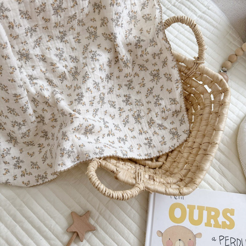 An Osmanthus floral print crinkled muslin blanket folded in a wicker basket, next to a children's book.