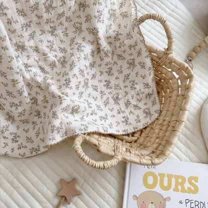 An Osmanthus floral print crinkled muslin blanket folded in a wicker basket, next to a children's book.