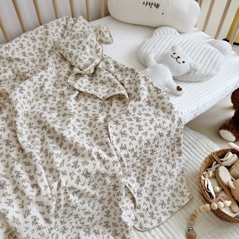 An Osmanthus floral print crinkled muslin blanket spread out in a crib, with a teddy bear toy, highlighting its use as a baby blanket.