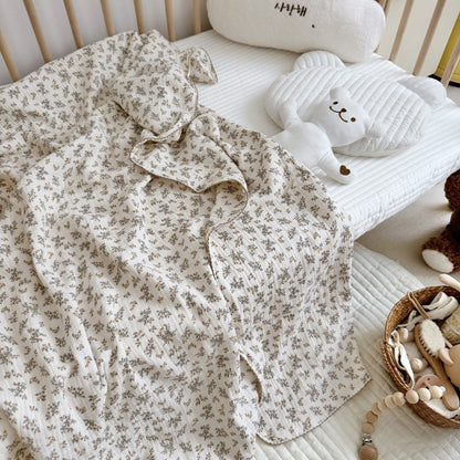 An Osmanthus floral print crinkled muslin blanket spread out in a crib, with a teddy bear toy, highlighting its use as a baby blanket.