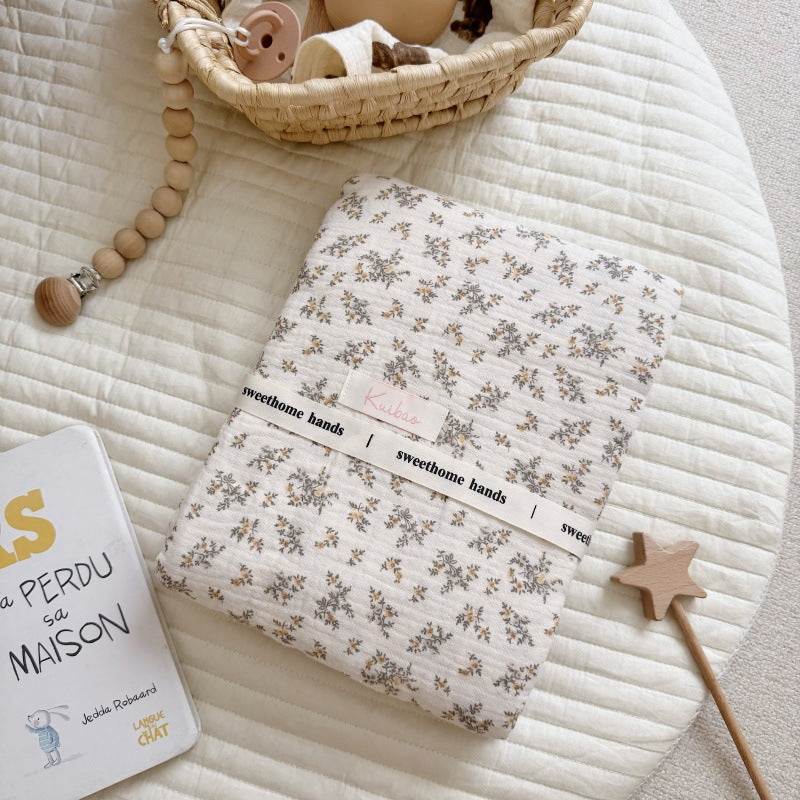 A neatly folded Osmanthus floral print crinkled muslin blanket tied with a brand ribbon, placed on a round cotton mat, showing the packaging.