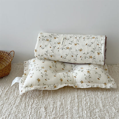 The yellow floral muslin receiving blanket and matching pillow set on a textured rug.