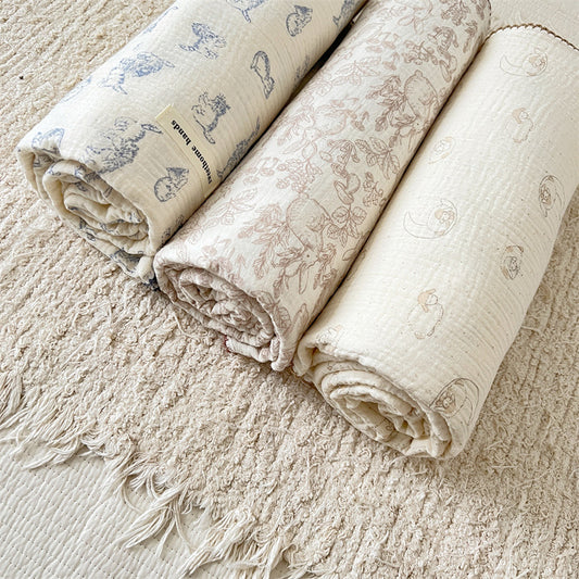 Rolled cute animal muslin blankets in lamb, kitty, and woodland designs on cream rug