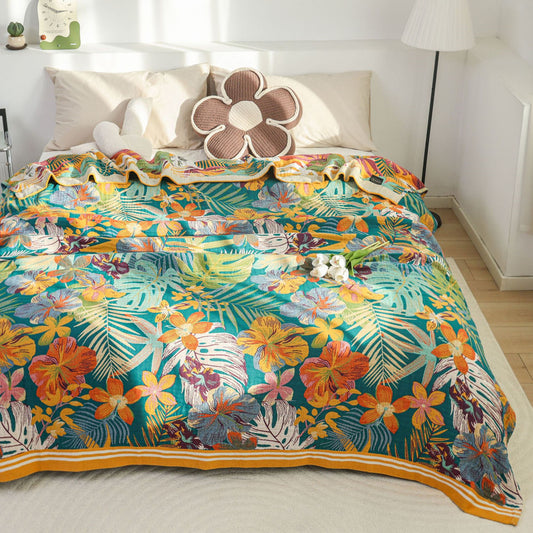 A front view of a bed covered with a colorful tropical paradise throw blanket featuring a mix of orange flowers and green leaves, with matching decorative pillows.