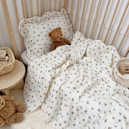 Teddy bear tucked into crib with comforter