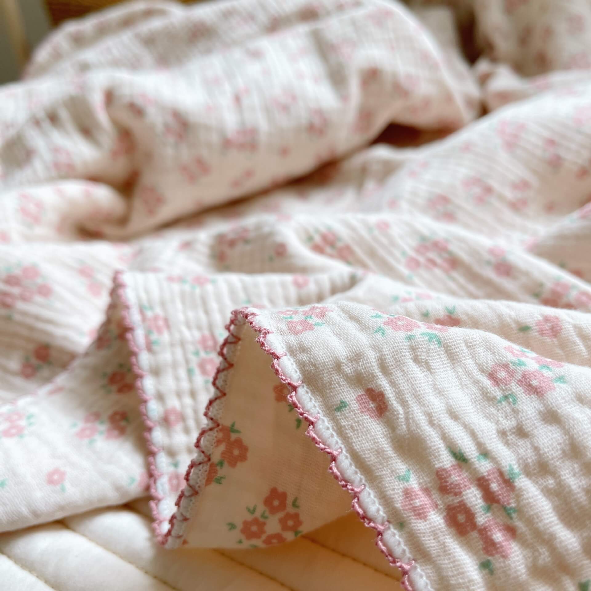 Close-up of the vintage floral cotton muslin baby blanket in carmine pink, showing the detailed print and frill trim.
