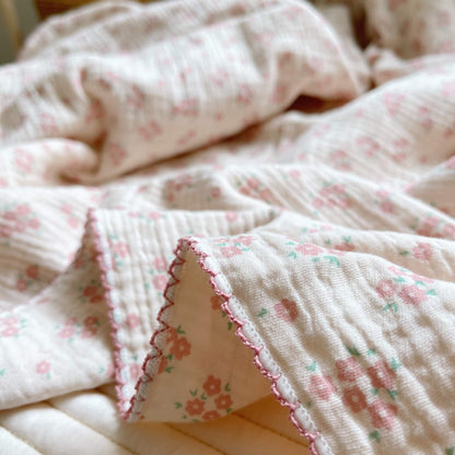 Close-up of the vintage floral cotton muslin baby blanket in carmine pink, showing the detailed print and frill trim.