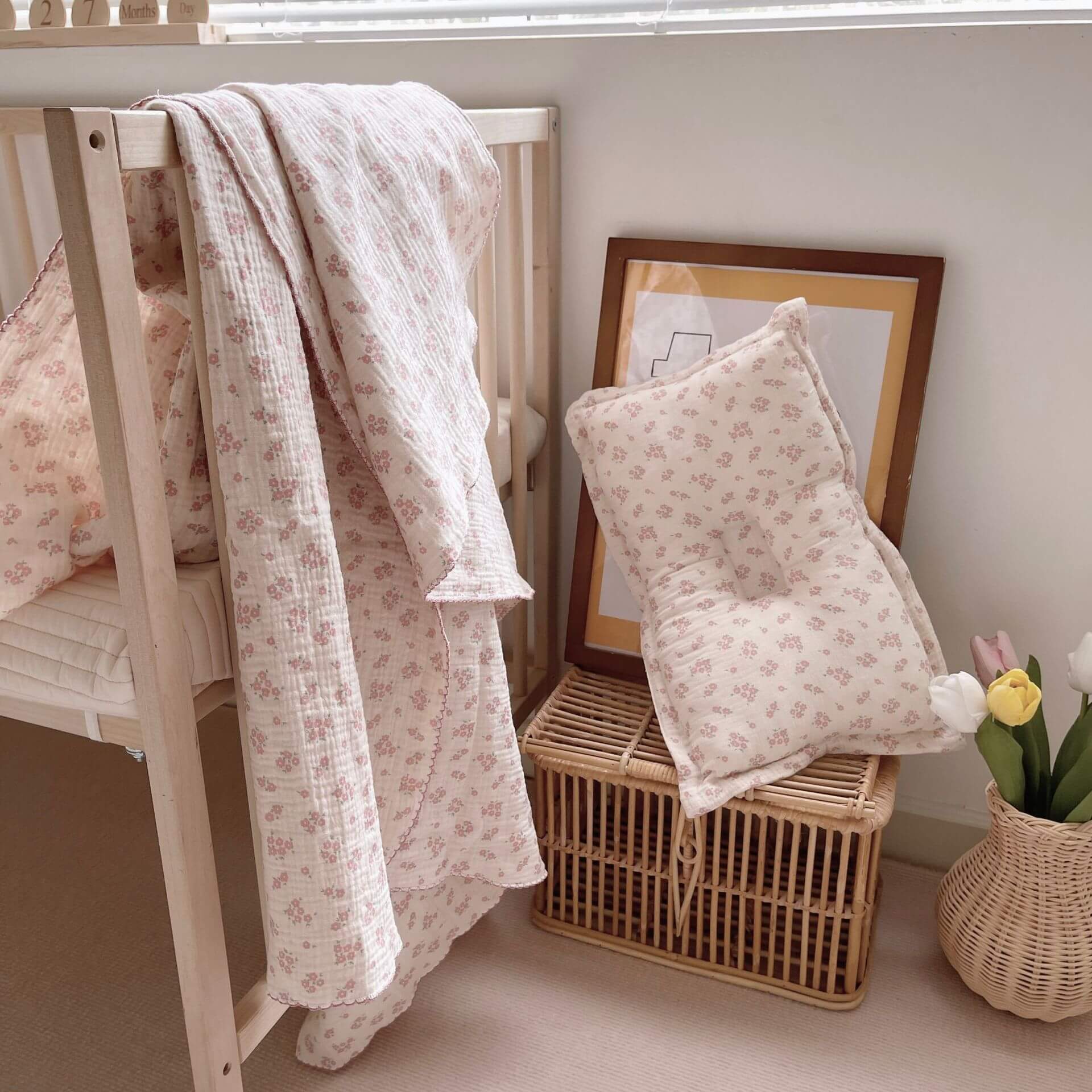 Vintage floral muslin baby blanket draped over a crib, with a matching pillow on a wicker chest