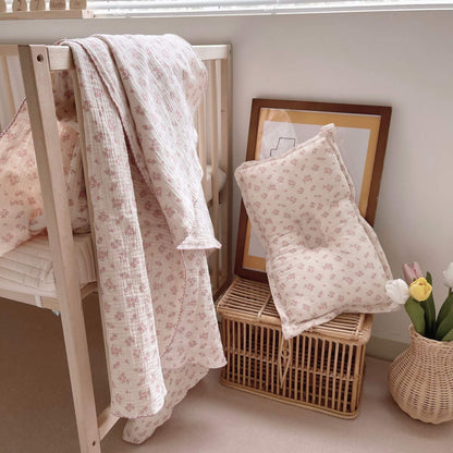 Vintage floral muslin baby blanket draped over a crib, with a matching pillow on a wicker chest