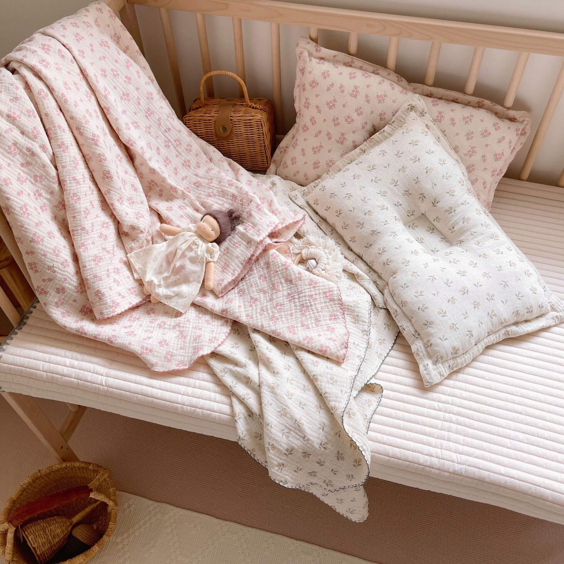 Vintage floral muslin baby blanket and two matching pillows on a wooden crib.