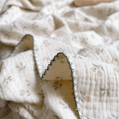 Close-up of a folded gauze swaddle blanket with a vintage floral pattern and a dark green scalloped trim